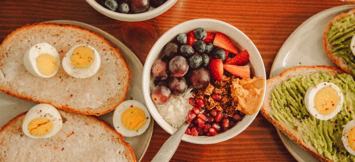 A fresh and vibrant breakfast flat lay featuring a yogurt bowl with fruits and toast with eggs and avocado.